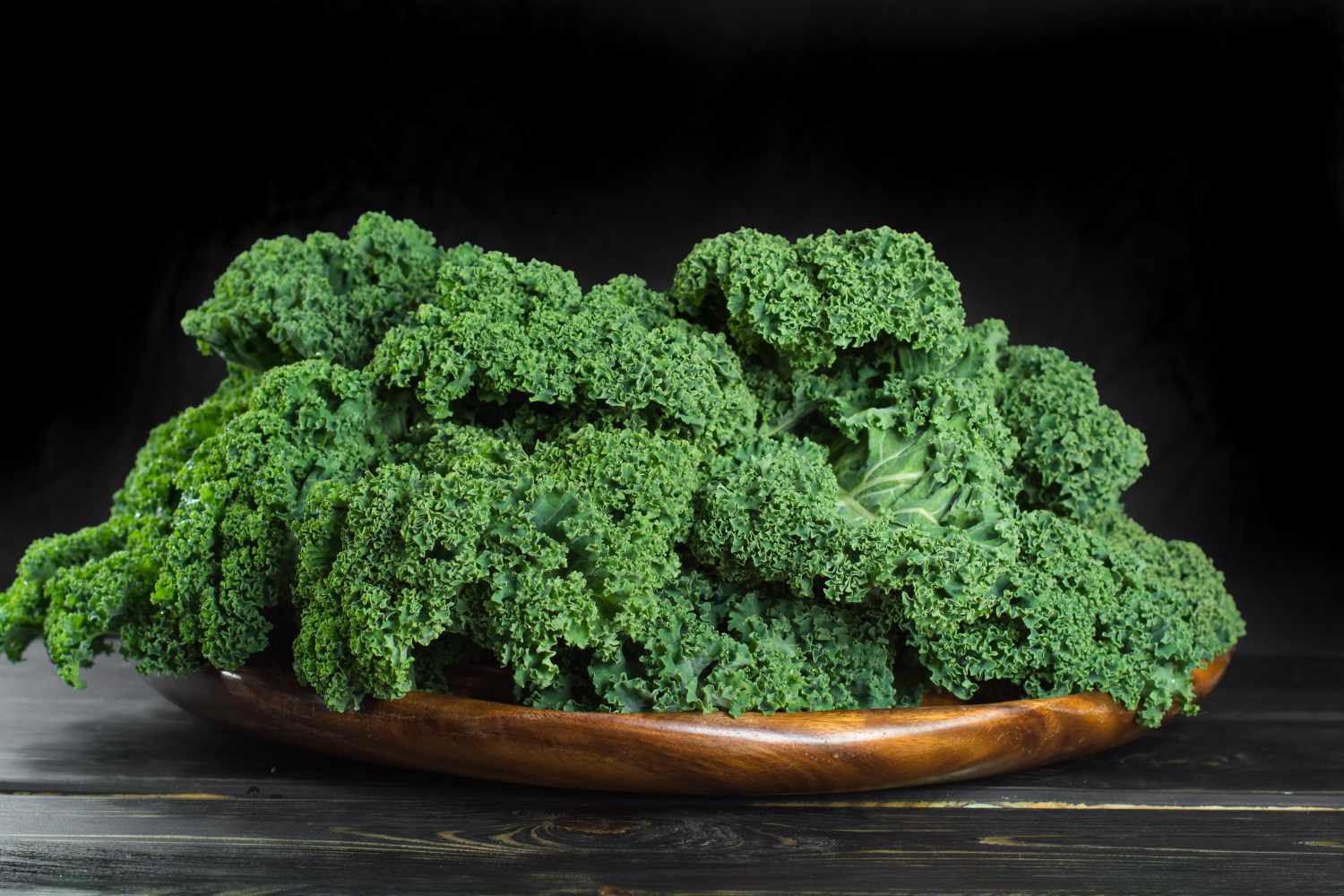 kale leaves in shallow wooden bowl with dark background
