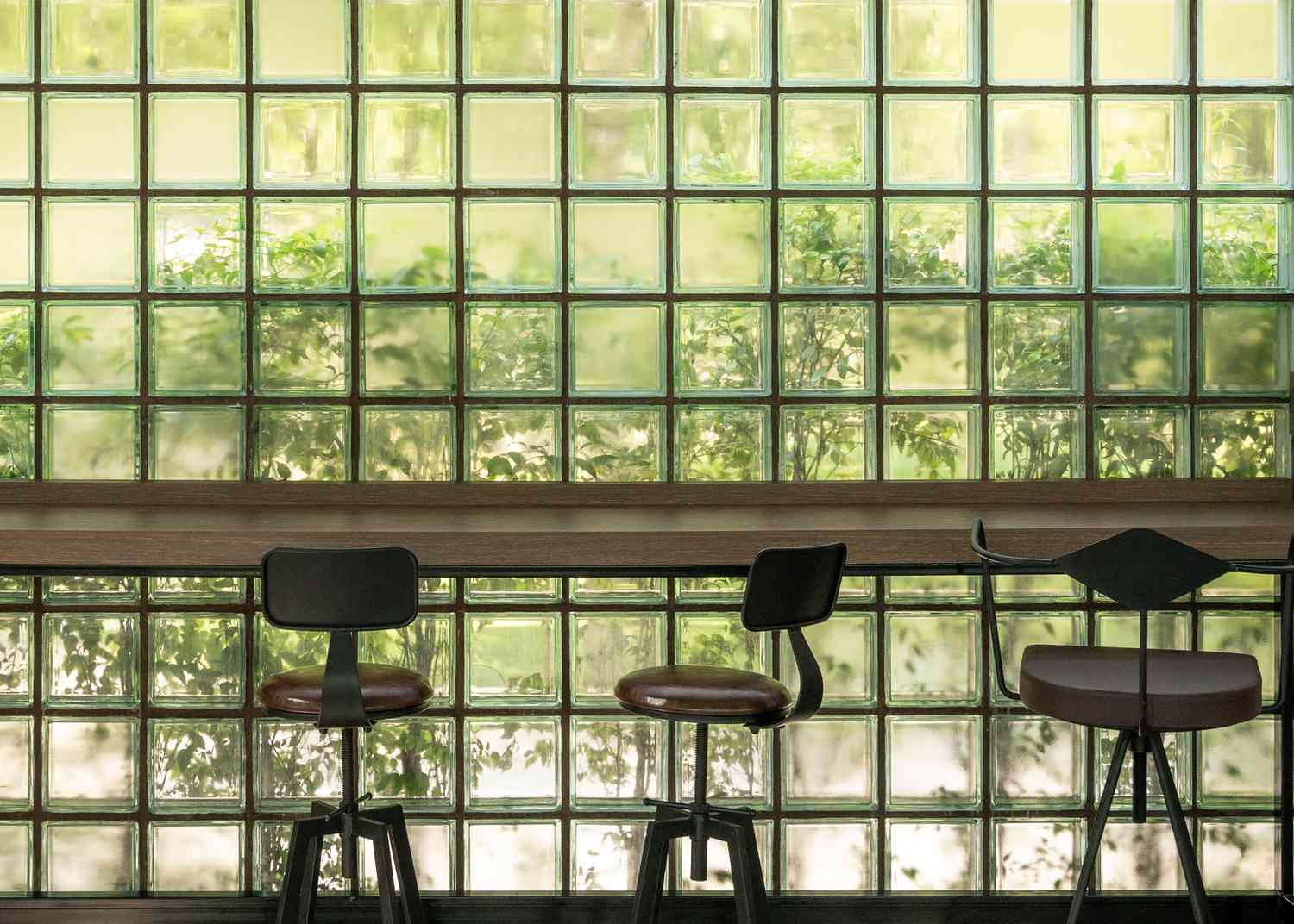 Row of chairs in front of a glass brick wall with greenery outside