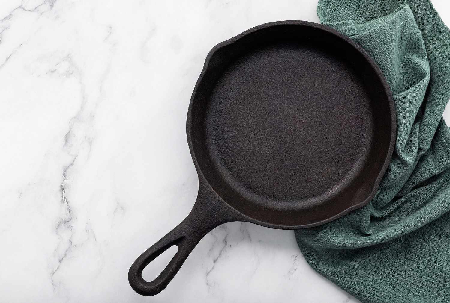 A cast iron skillet placed on a marble surface with a green cloth beside it