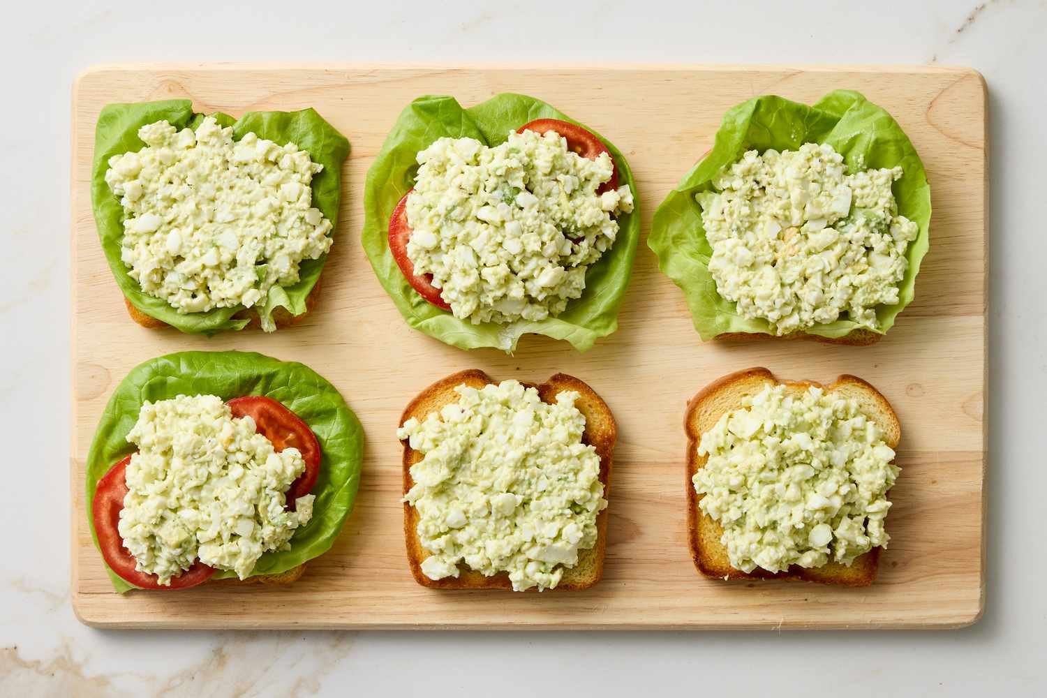 Egg salad sandwiches with lettuce and tomato on bread presented on a wooden board