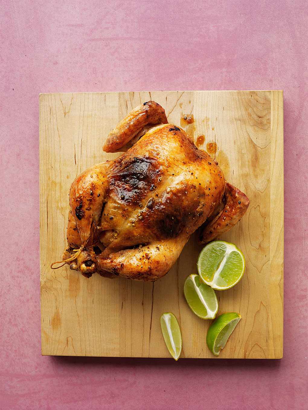 A whole roasted chicken shown on a wooden cutting board with lime wedges next to it
