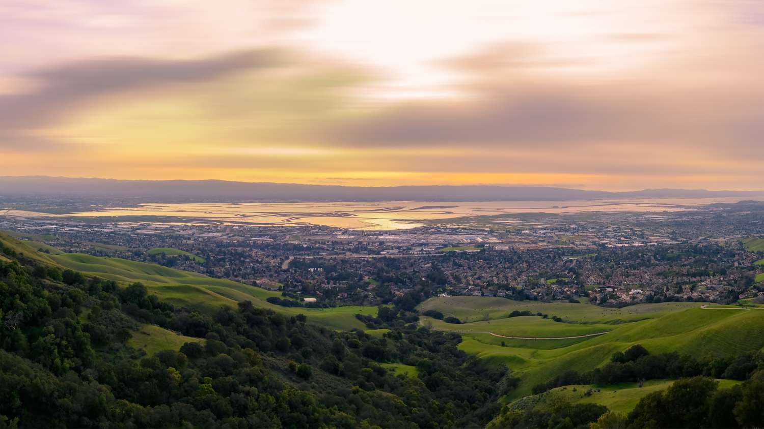 A cityscape surrounded by hills taken during sunset with a view of water bodies in the background