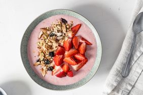 A smoothie bowl topped with granola and sliced strawberries placed on a table with a napkin and a spoon