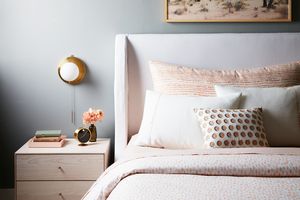 Neatly arranged bedroom with a bed side table with books a lamp and decorative pillows and flowers