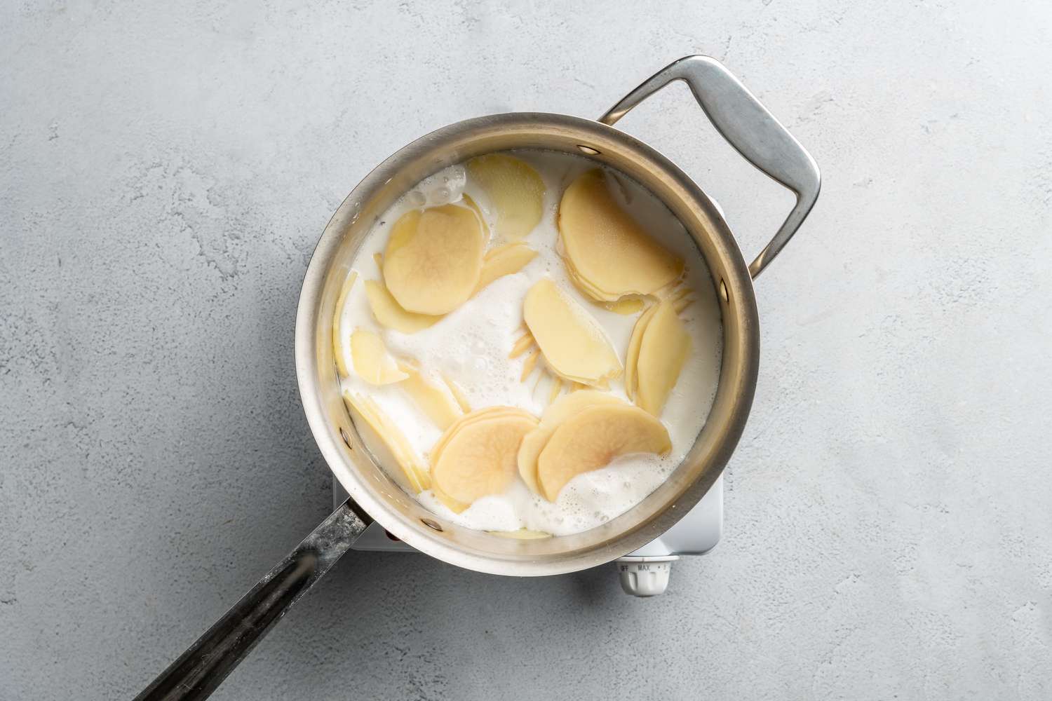 sliced potatoes cooking in milk for scalloped potatoes