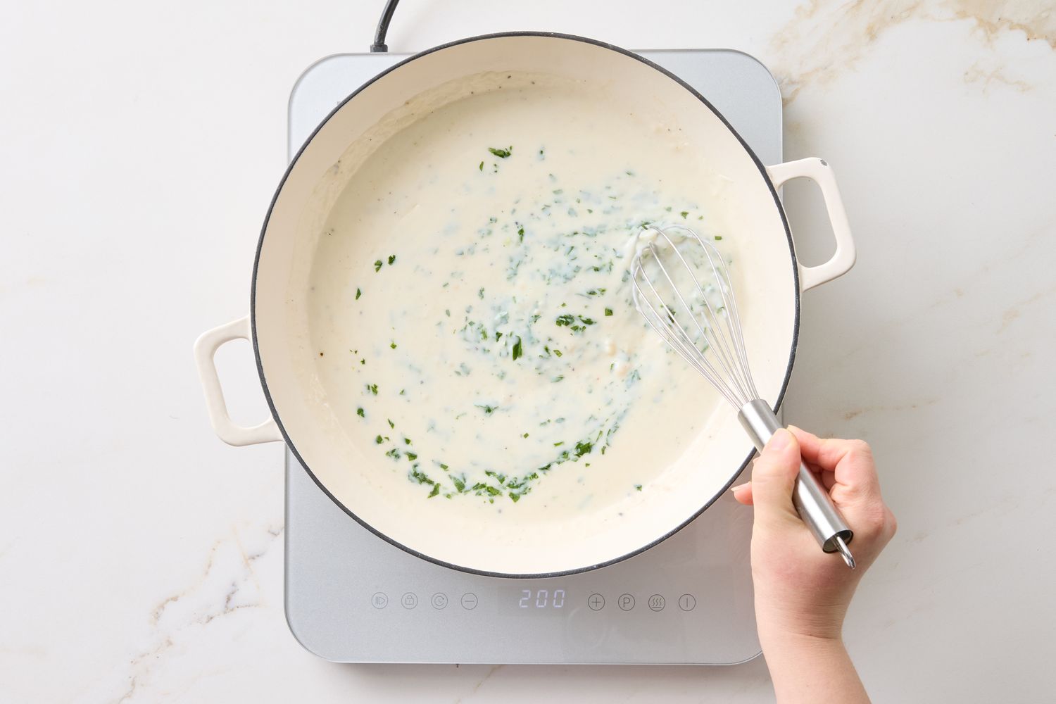 A hand whisking sauce in a pot on an induction stove