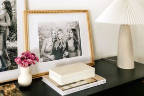 Framed photograph of three women on a table alongside decorative objects such as a lamp books and a white vase with pink flowers