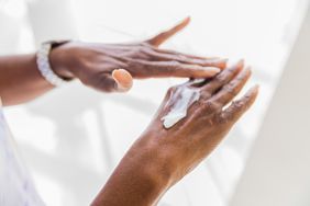Hands of a mature black woman, applying cream to keep them moisturized