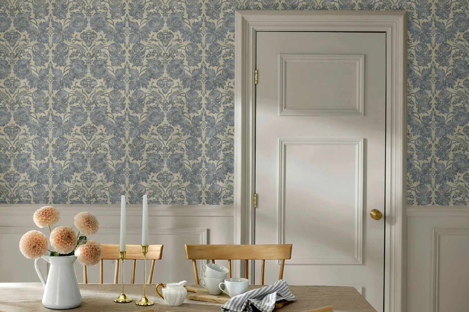 Dining table with flowers and tableware in front of a closed door and patterned wallpaper