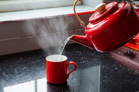A kettle pouring hot water into a mug on a counter with steam rising from the cup