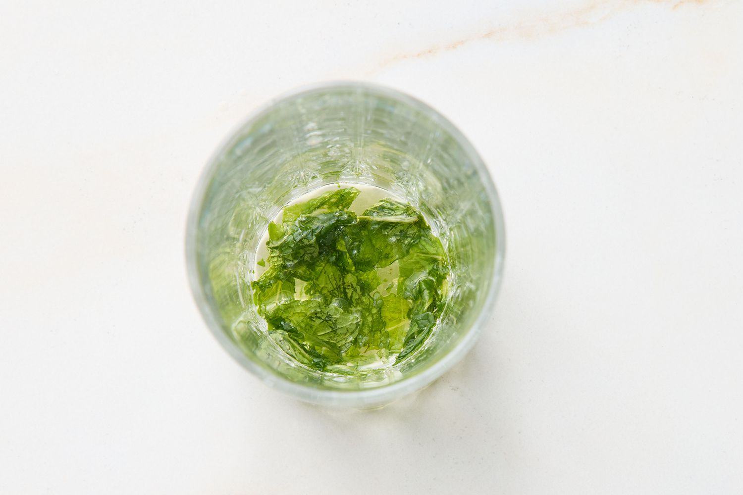 Glass containing muddled mint leaves viewed from above, ingredients for a mojito cocktail