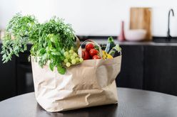 A grocery bag on a table containing fresh vegetables and fruits