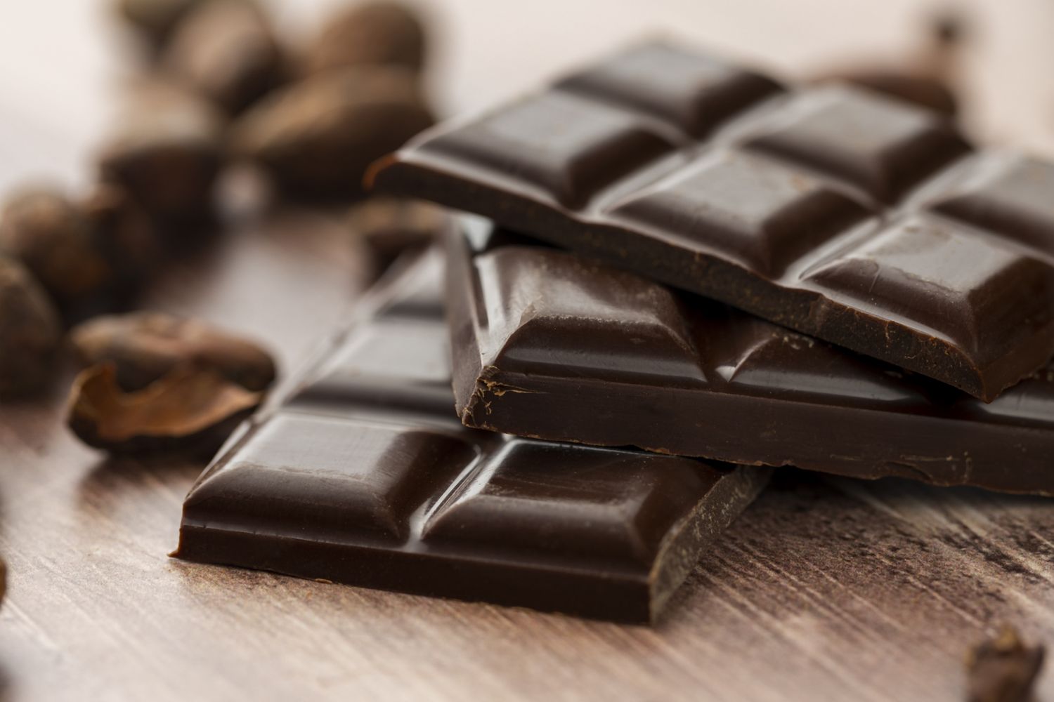 Closeup of stacked chocolate bars on a wooden surface surrounded by cocoa beans