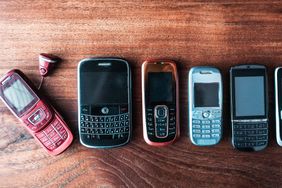 A row of old cell phones placed on a wooden surface displaying a variety of designs and layouts
