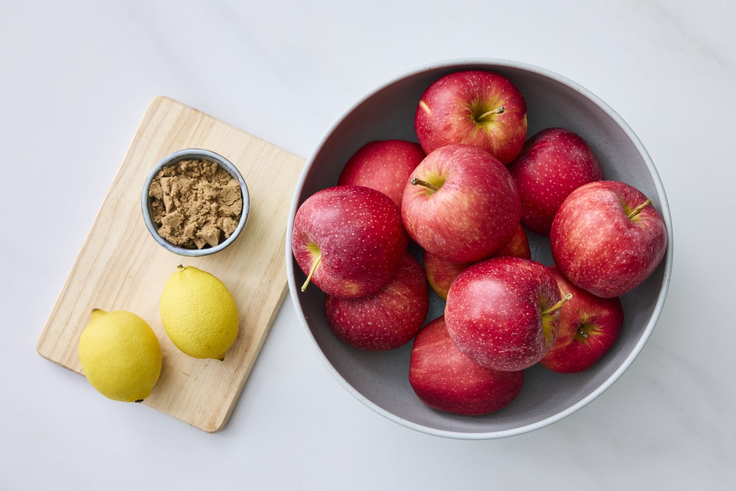 Ingredients including apples lemons and sugar displayed on a board and bowl