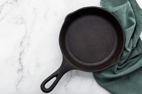 A cast iron skillet placed on a marble surface with a green cloth beside it