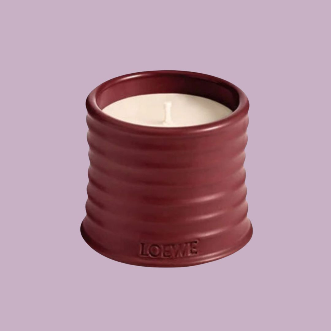 A candle in a red cylindrical ceramic holder with the brand name Loewe embossed on it