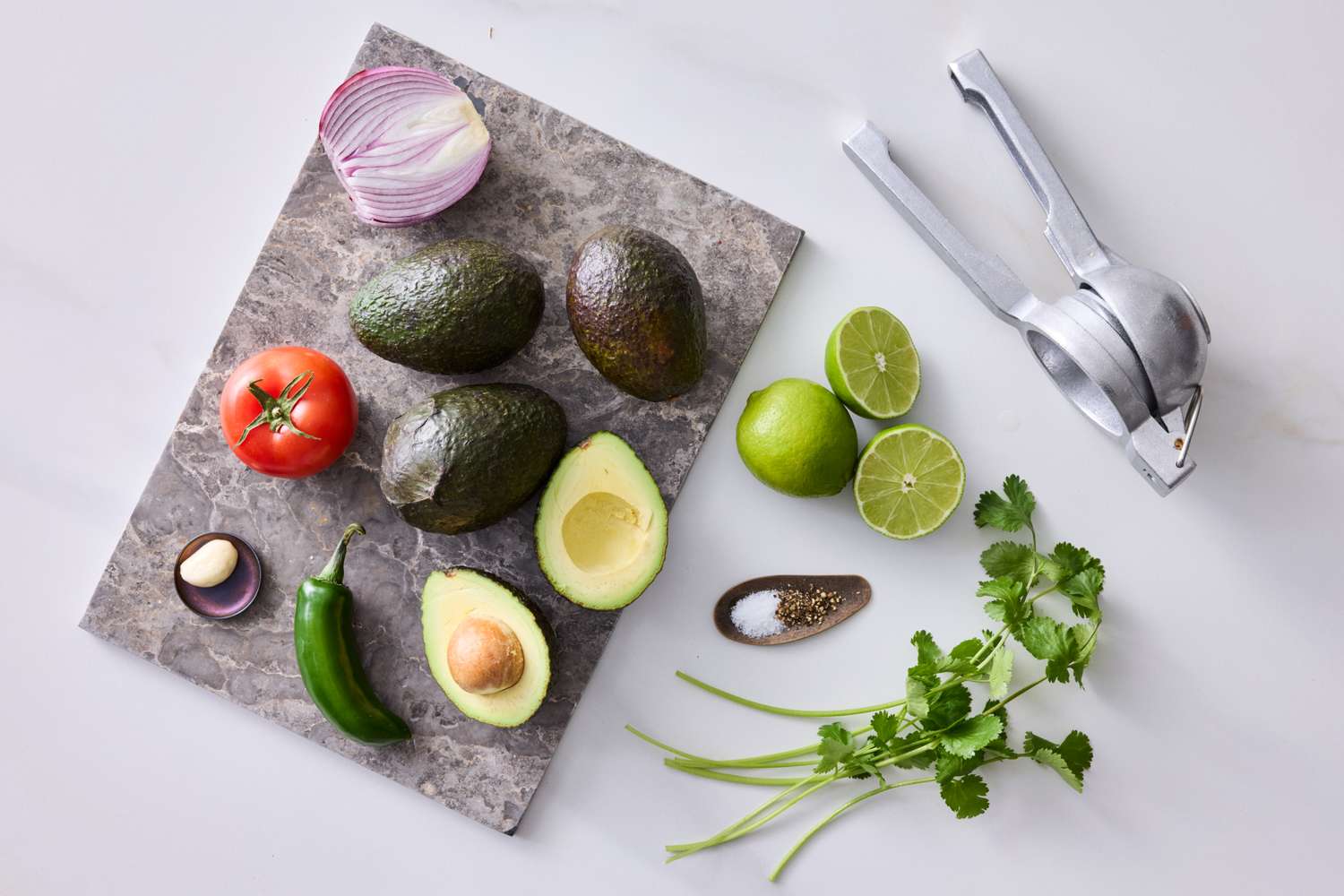 Ingredients for making guacamole including avocados a tomato red onion jalapeo lime garlic cilantro and seasoning