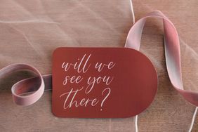 A card with the text will we see you there placed on fabric and next to a ribbon