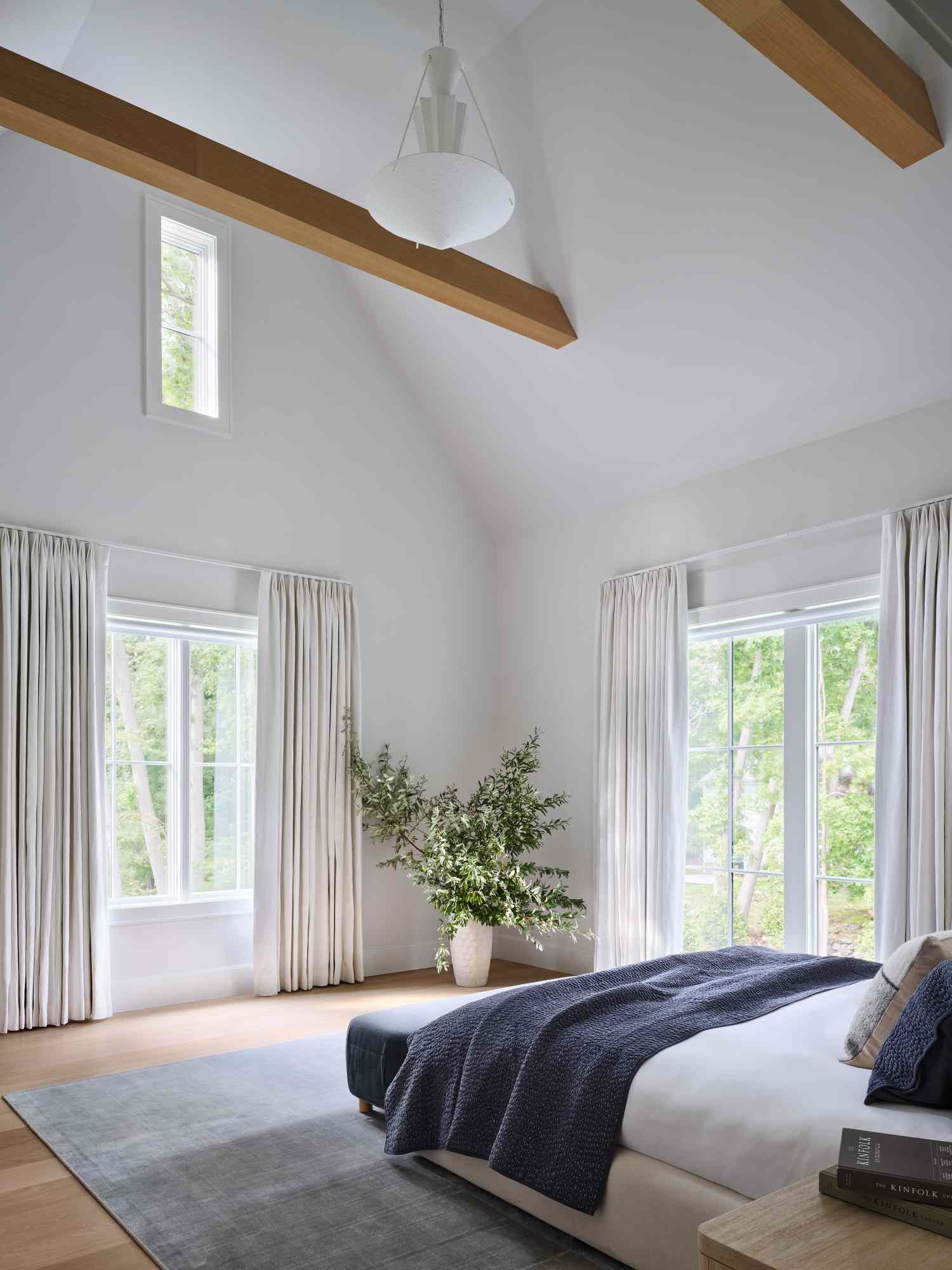 A tranquil modern bedroom with high ceilings, large windows, and natural light shining into the space