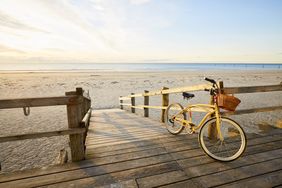 A bike with a basket parked on a wooden boardwalk leading to a beach