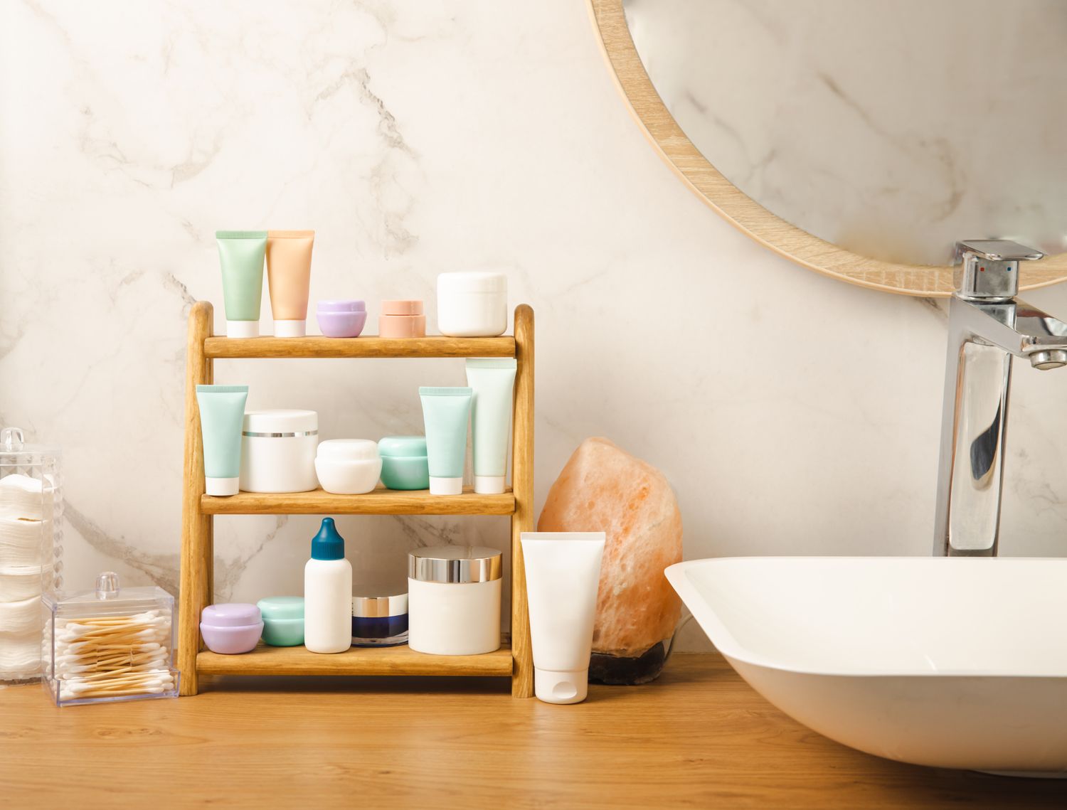 Bathroom counter with neatly arranged skincare products on a wooden rack next to a salt lamp and a sink