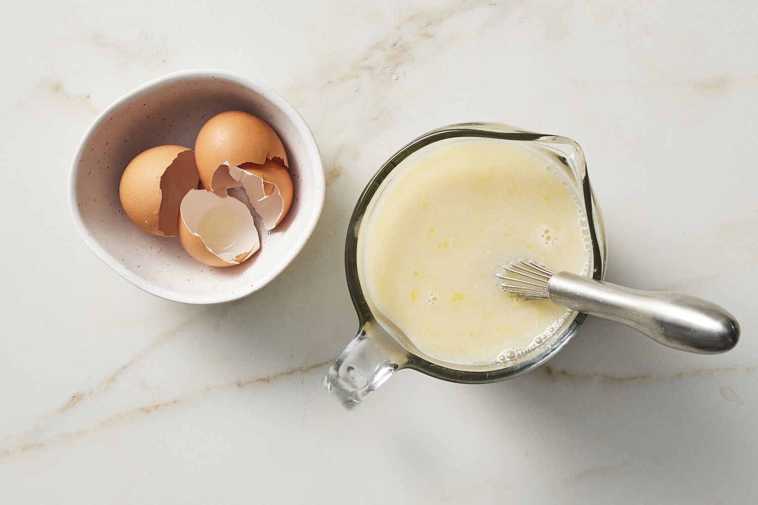 Cracked eggs shells next to glass cup of honey and milk and yeast