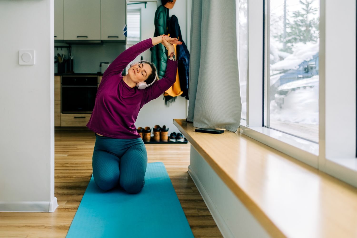 Person practicing yoga indoors on a mat stretching with arms overhead wearing headphones