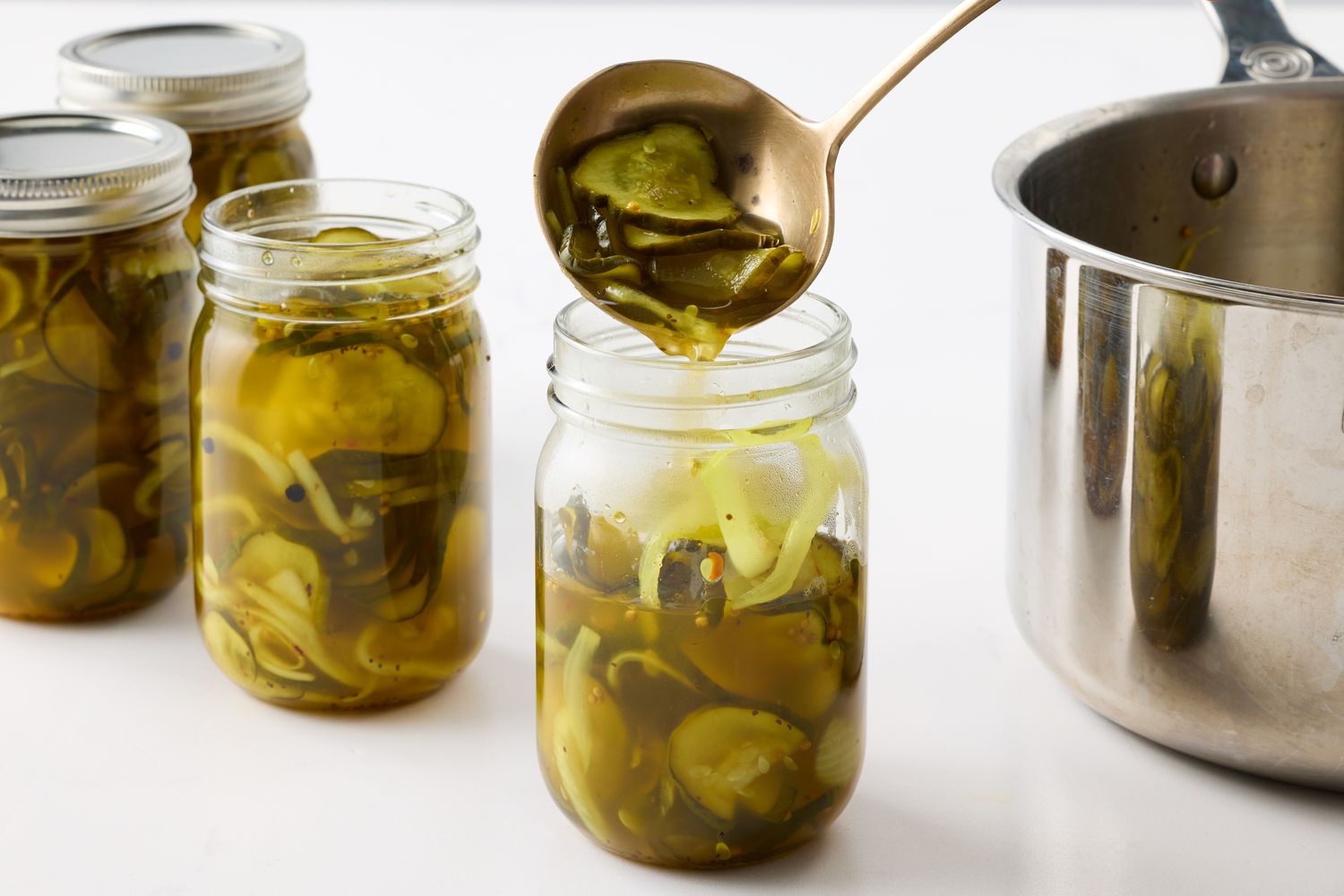 Jars of pickles being filled with a ladle from a pot