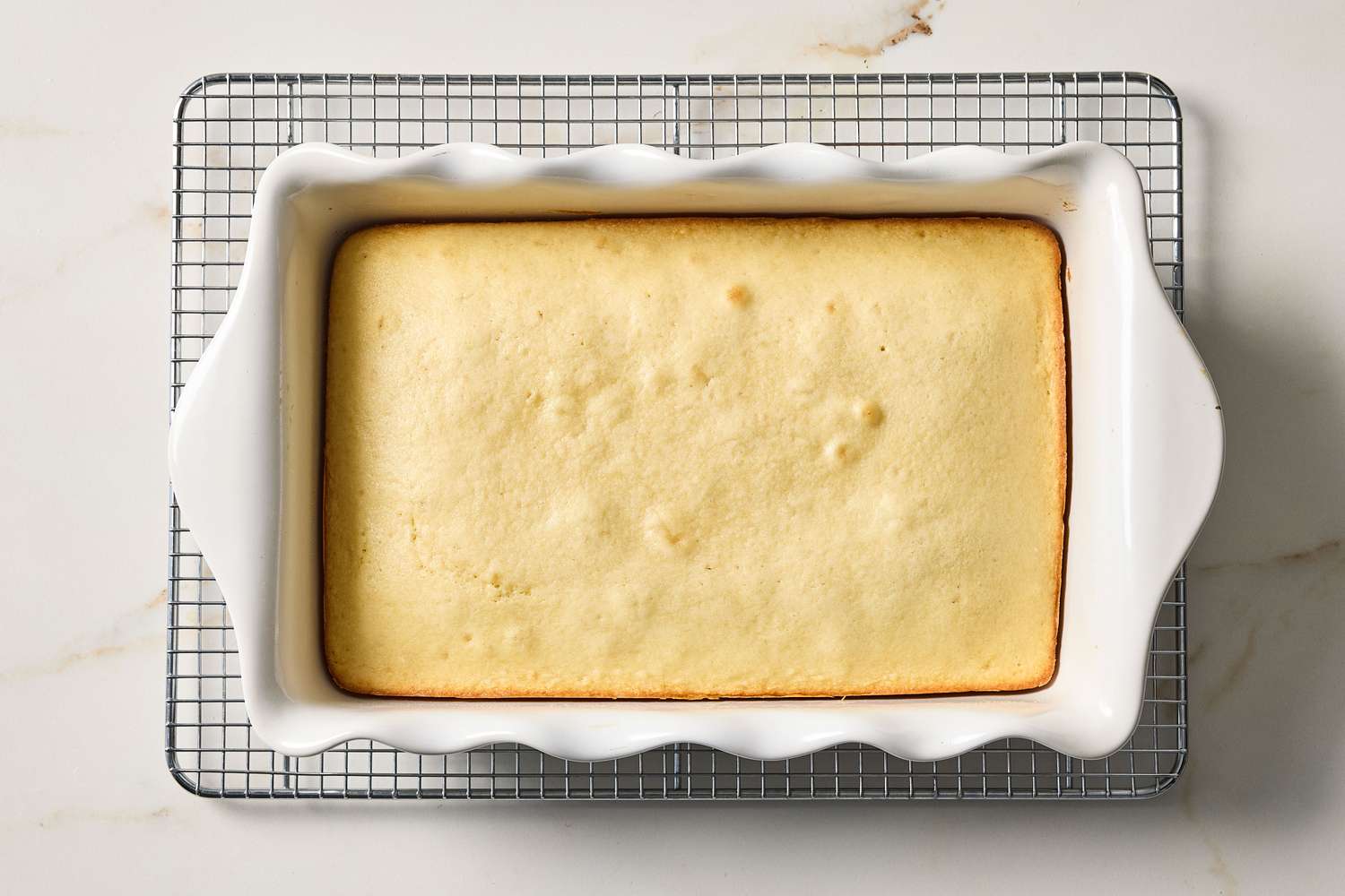 Baked vanilla sheet cake in a white rectangular dish on a cooling rack