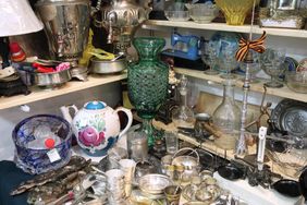 Assorted vintage glassware decorative items and various utensils displayed on cluttered shelves