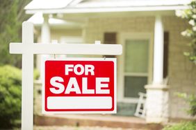 A red and white For Sale sign in front of a house focus on the sign