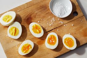 Hardboiled eggs sliced on a wooden cutting board next to a small bowl of salt