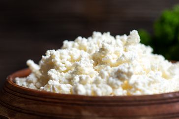 A wooden bowl filled with cottage cheese closeup view
