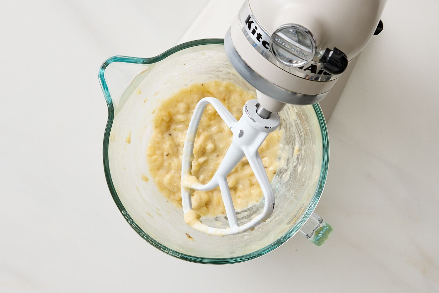 Banana mixture in a glass bowl on a stand mixer with a beater attachment