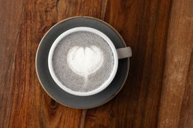 A cup of black sesame latte with latte art on a wooden table