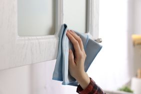Woman with microfiber cloth cleaning white cabinet in kitchen