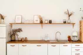 A minimalist kitchen counter with wooden details a shelf with decor and a coffee maker on the right side