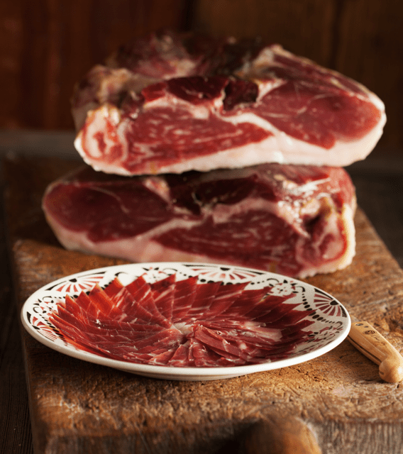 slices of cinco jotas jamon on a plate with jamon behind