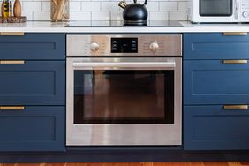 Modern kitchen with a builtin stainless steel oven centered below a countertop surrounded by dark cabinets and a tile backsplash