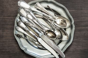 A stack of various utensils including spoons forks and knives on a plate