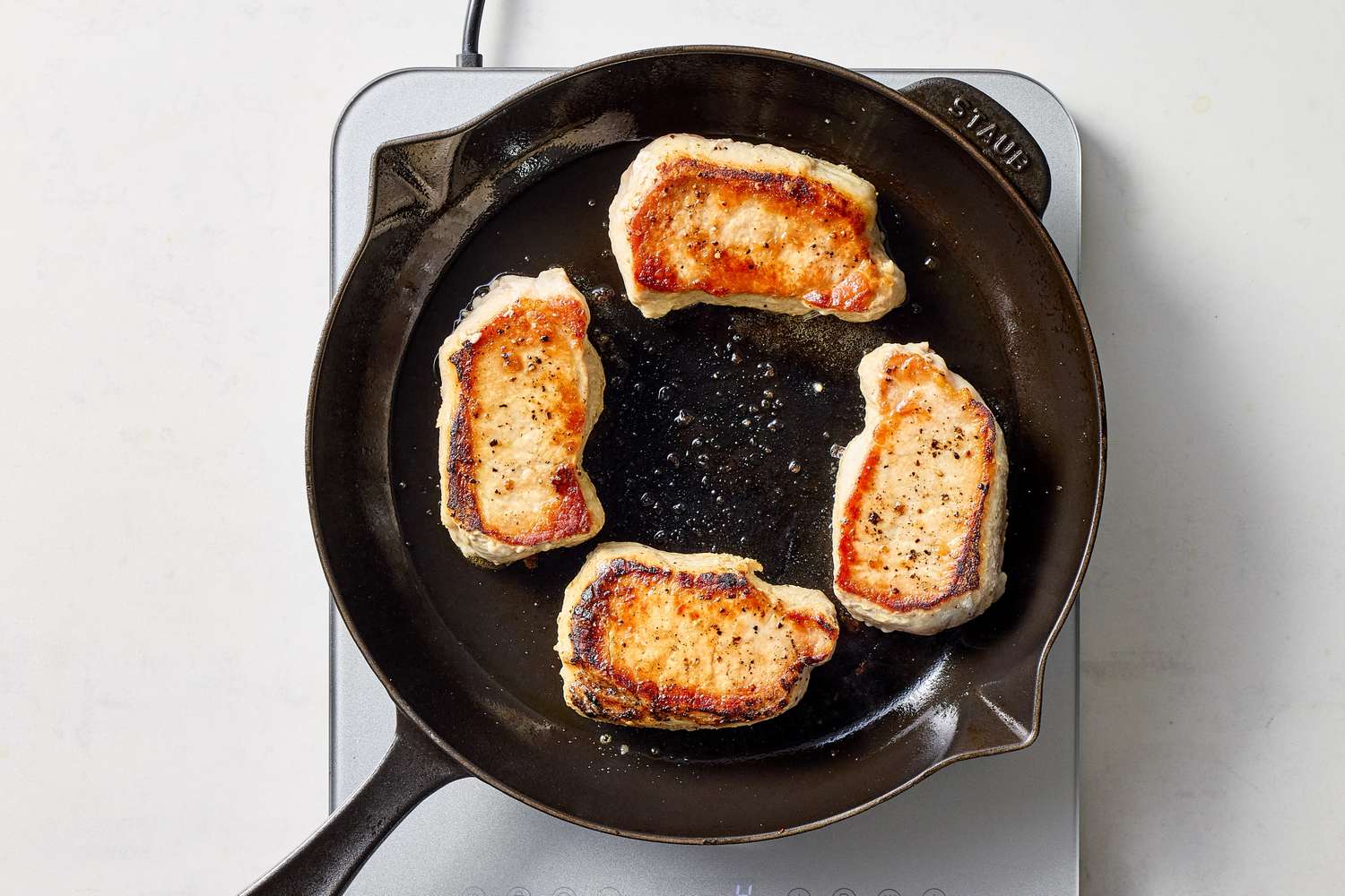 Four pork chops cooking in a cast iron skillet on a stovetop