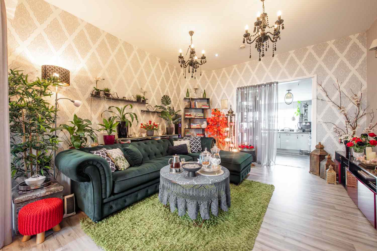 A living room with a green velvet sofa, indoor plants, chandeliers, and modern decor