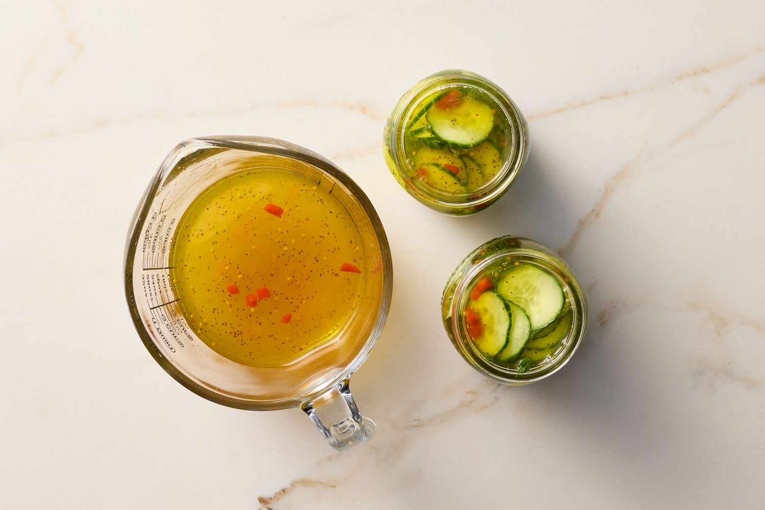 Jarred pickles alongside a measuring cup containing liquid seasoning mixture