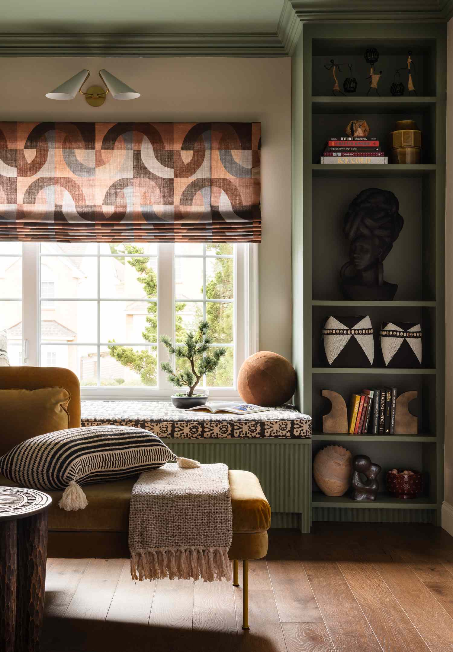 A cozy living room with a chair throw blanket and decorative bookshelf by a window