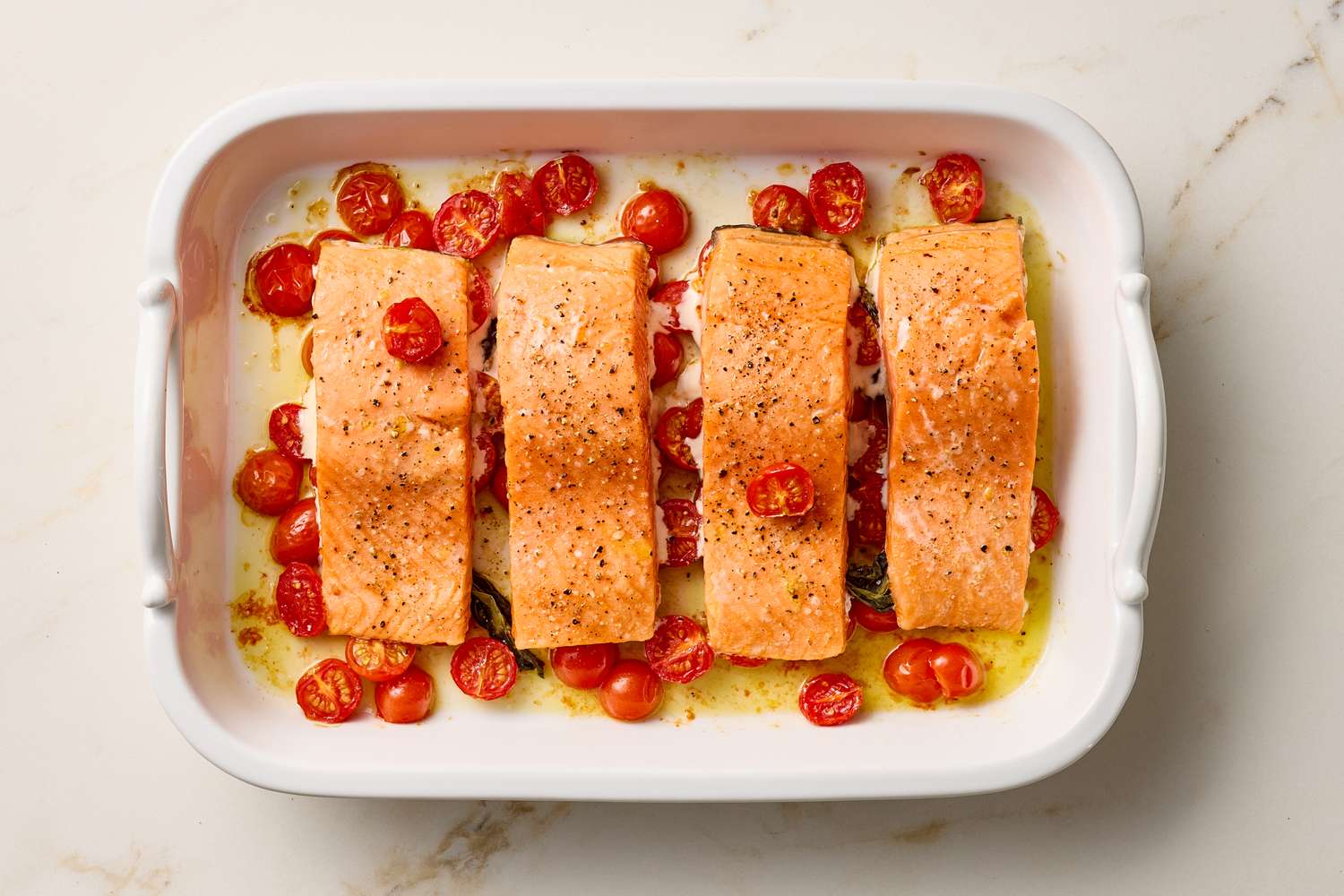 Baked salmon fillets served in a white dish with roasted cherry tomatoes