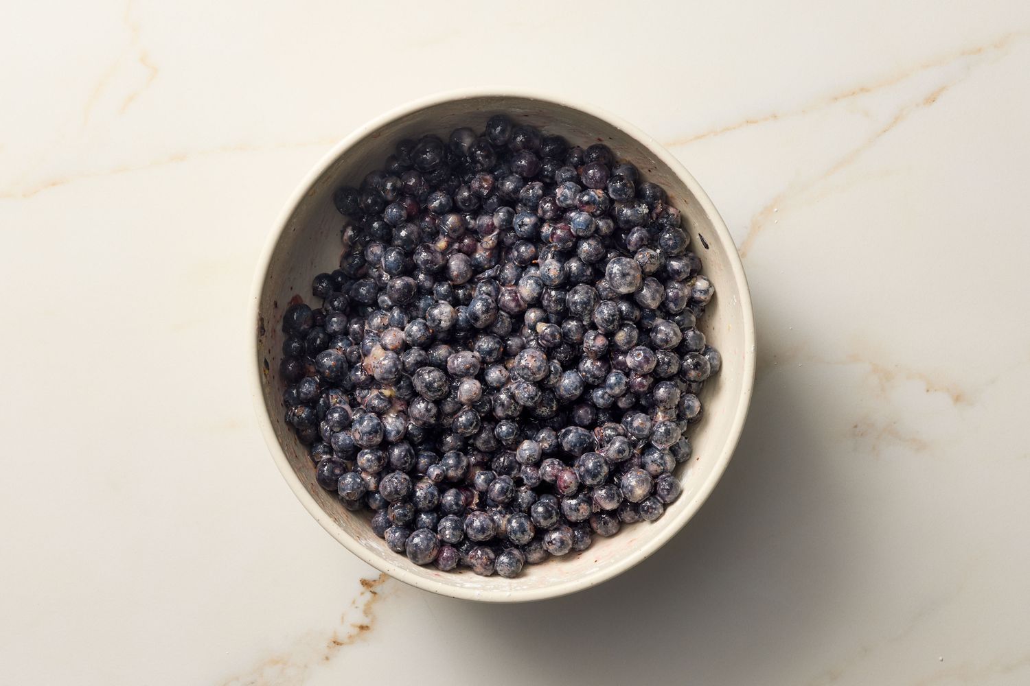 A bowl filled with blueberries, resting on a marble surface