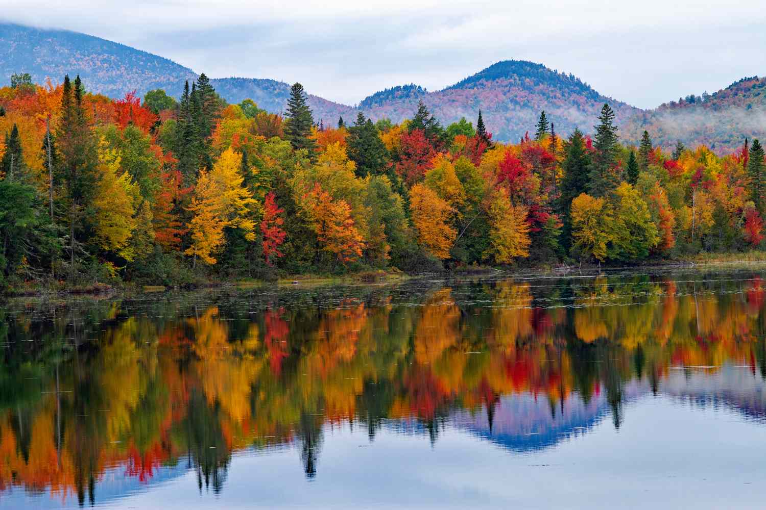 Autumn foliage reflected in a calm lake with mountains in the background