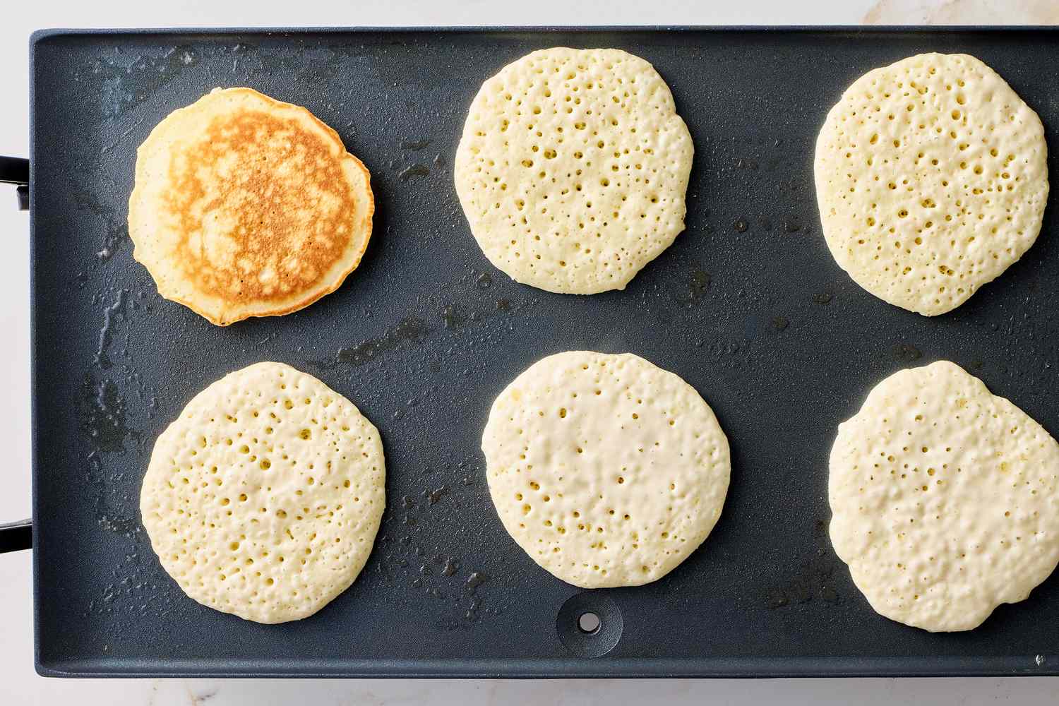 Pancakes cooking on a griddle with one pancake flipped