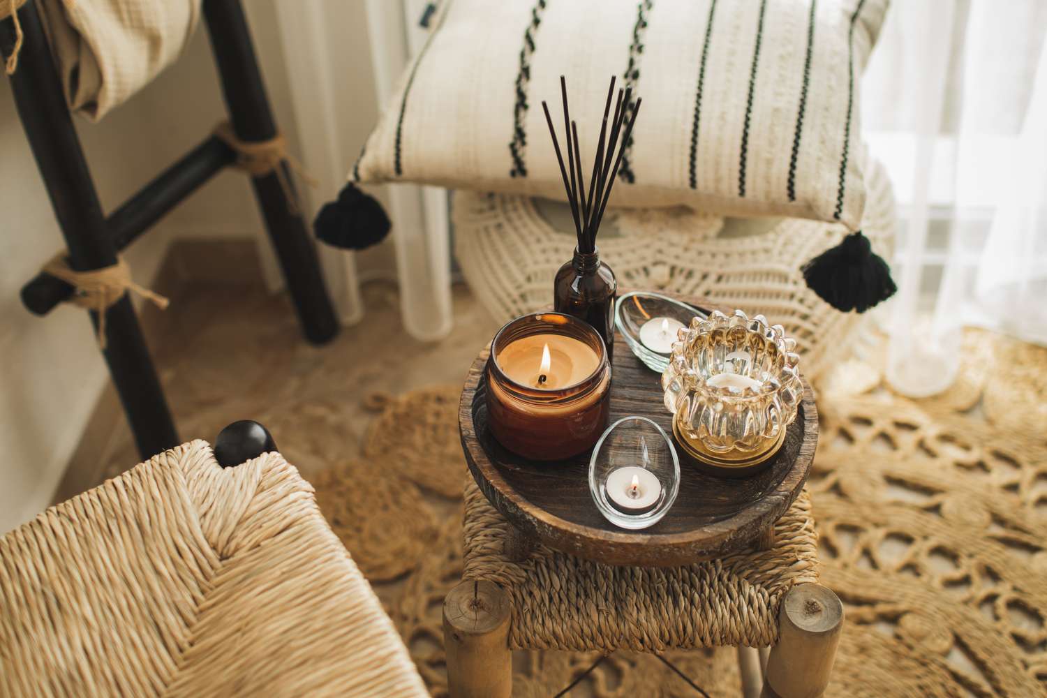 A wooden stool with lit candles and incense arranged on a tray placed in a cozy living space with woven decor